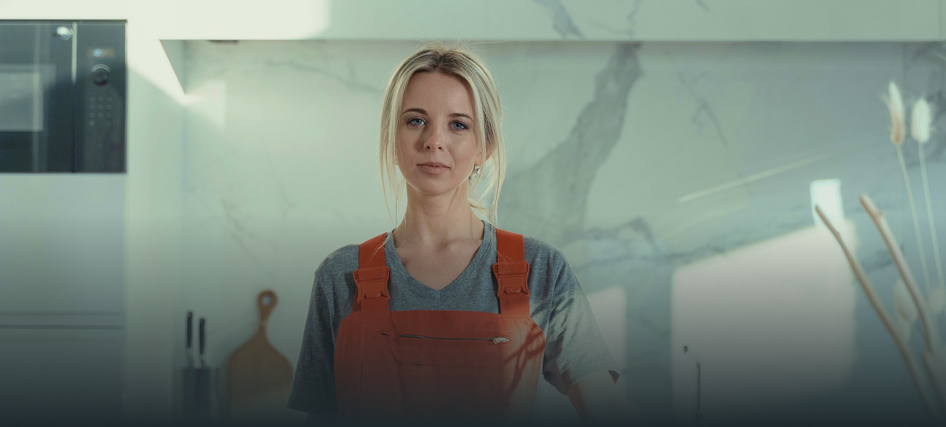 Rengøringsassistent i orange arbejdstøj i et lyst, moderne køkken